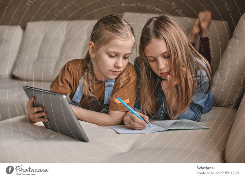 Zwei schöne Schwestern machen während der Quarantäne ihre Hausaufgaben. Kinder verwenden zum Lernen Geräte. Bildung, Fernunterricht, Heimunterricht während der Quarantäne
