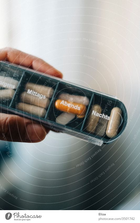 Eine Person hält eine Medikamentenbox, in die verschiedene Tabletten und Pillen für die unterschiedlichen Tagseszeiten sortiert sind, in der Hand
