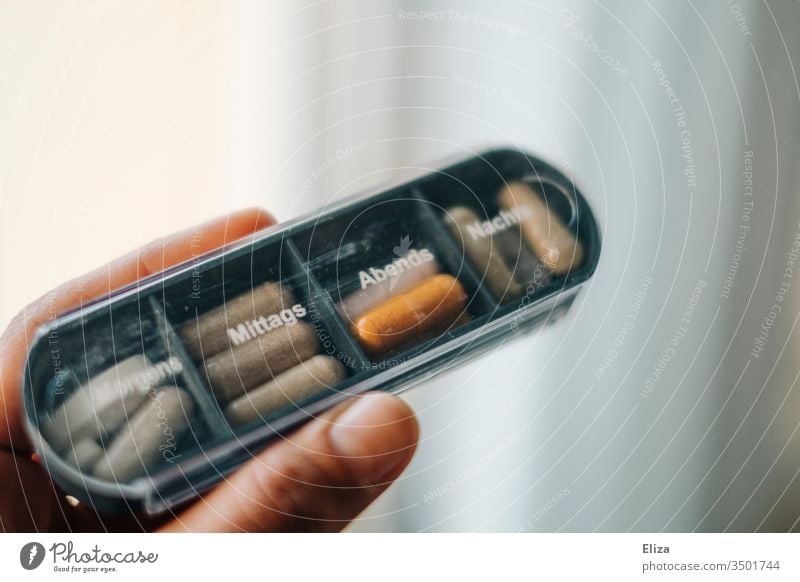 Eine Person hält eine Medikamentenbox, in die verschiedene Tabletten und Pillen für die unterschiedlichen Tagseszeiten sortiert sind, in der Hand