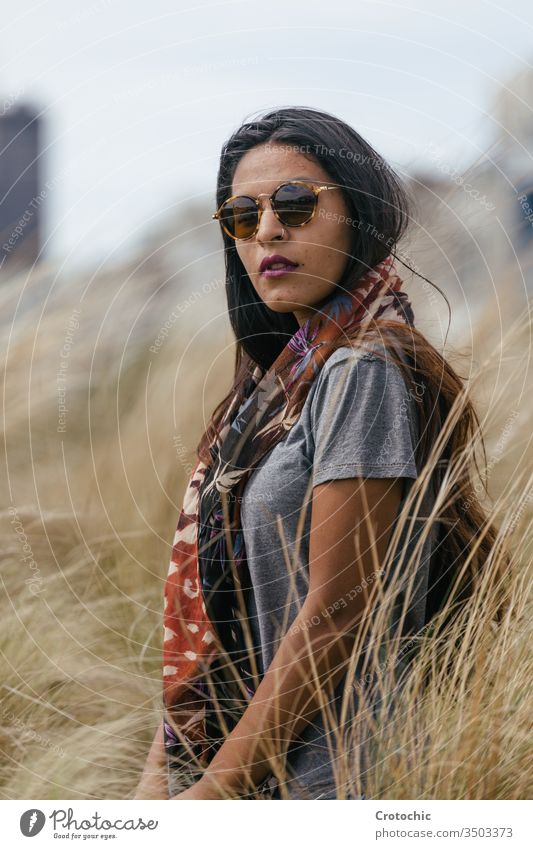 Bildnis einer brünetten Frau mit Sonnenbrille, die in einem Weizenfeld einen Schal am Hals trägt Schönheit arabisch Porträt Feld wild drehen. Gesicht