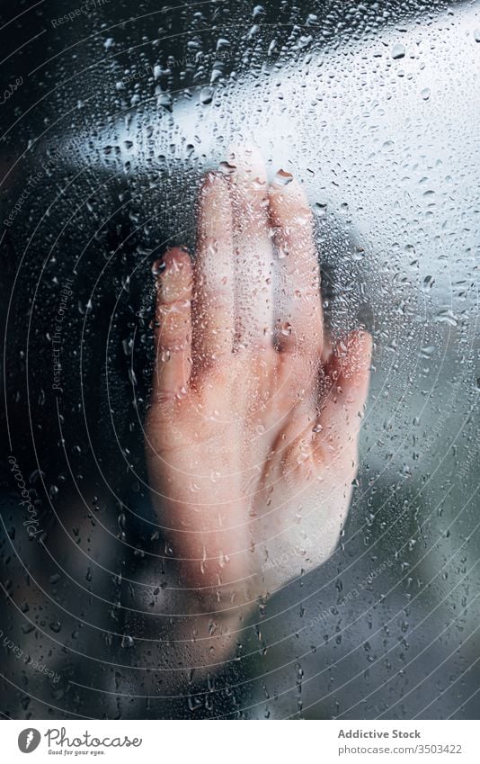 Anonyme Person, die ein Fensterglas berührt Hand heimwärts Isolation verzweifelt nass Coronavirus einsam Depression Einsamkeit Regen Problematik Konzept