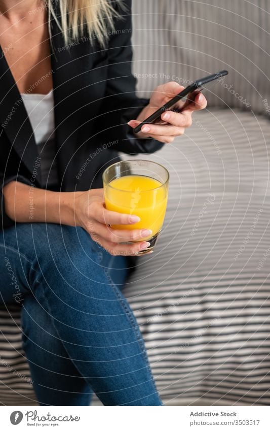 Anonyme Frau trinkt Saft und benutzt Smartphone auf dem Sofa benutzend heimwärts Handy trinken ruhen soziale Netzwerke räkeln Gesundheit sitzen frisch orange