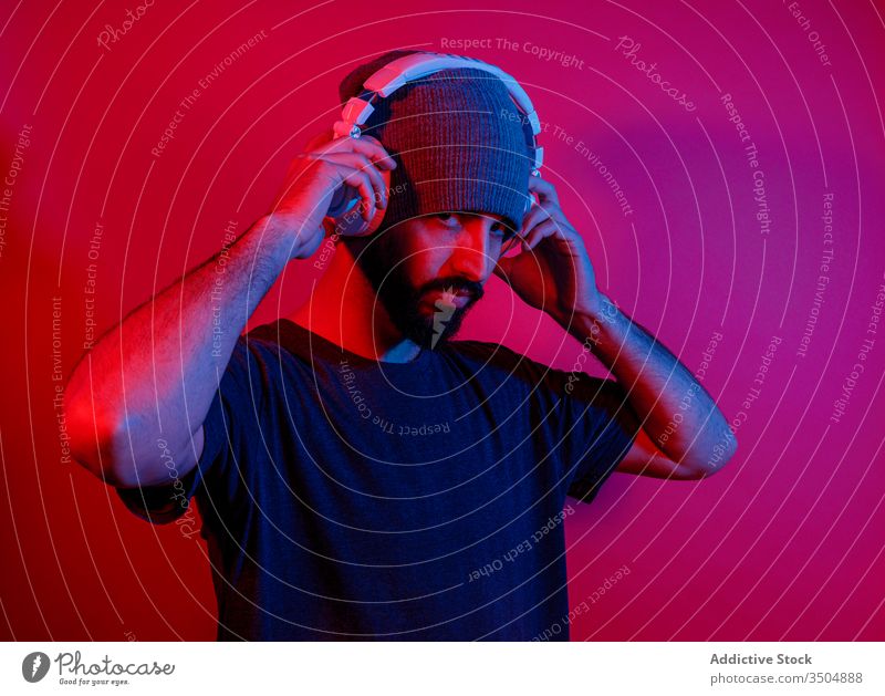 Bärtiger Mann hört Musik über Kopfhörer zuhören Stil modern Vollbart Rotlicht hell Nachtleben männlich leuchten neonfarbig Gerät pulsierend Apparatur Klang