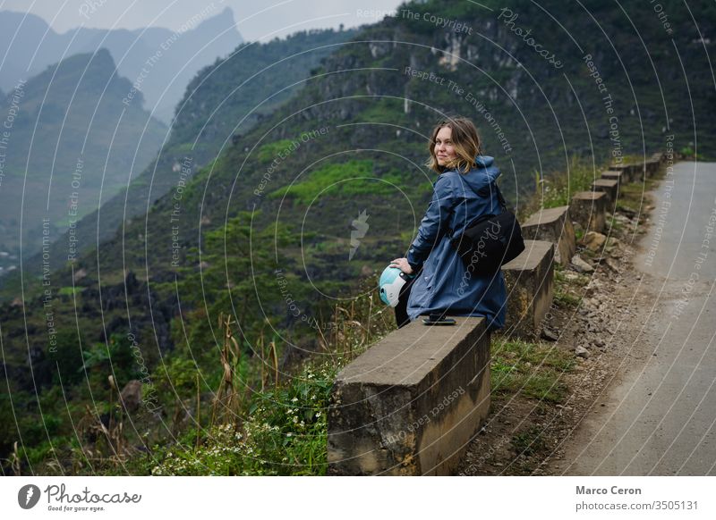 Junge Frau am Rande einer Bergstraße sitzend, Attraktive Bakpackerin, die mit dem Motorrad durch Nordvietnam fährt. Berge u. Gebirge Person Straße reisen Natur