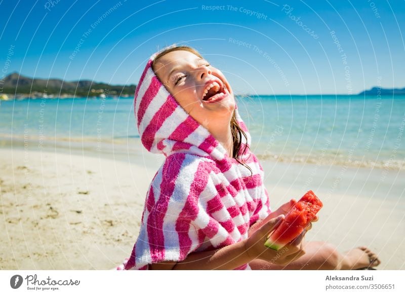Süßes fröhliches kleines Mädchen isst Wassermelone und lacht am Sandstrand. Türkisfarbenes Meer, blauer Himmel, sonniger Sommertag. Mallorca, Spanien Aktivität