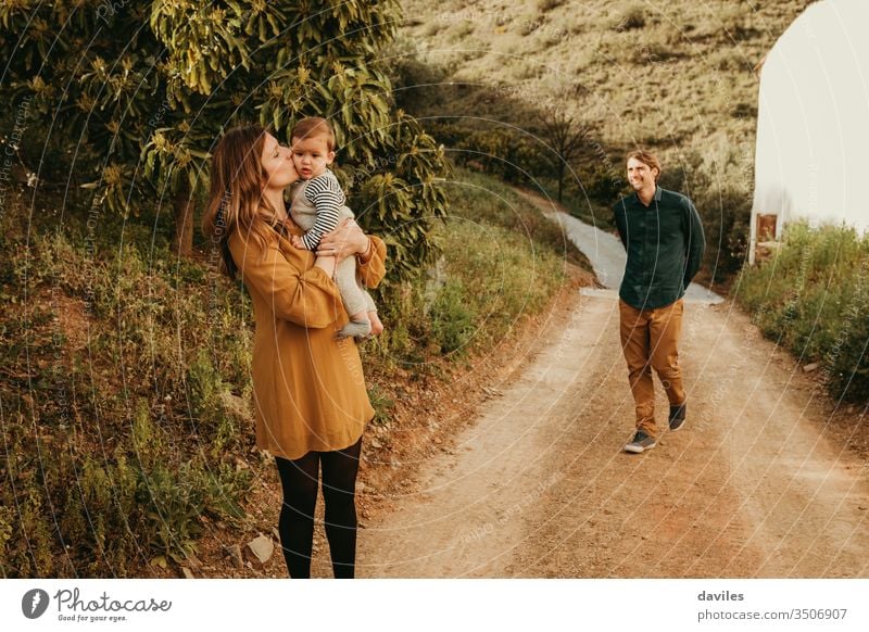 Eine Frau, die ihren kleinen Sohn in der Natur küsst, steht im Weg, während der Mann sich ihnen mit einem Lächeln nähert. Landschaft liebende Familie