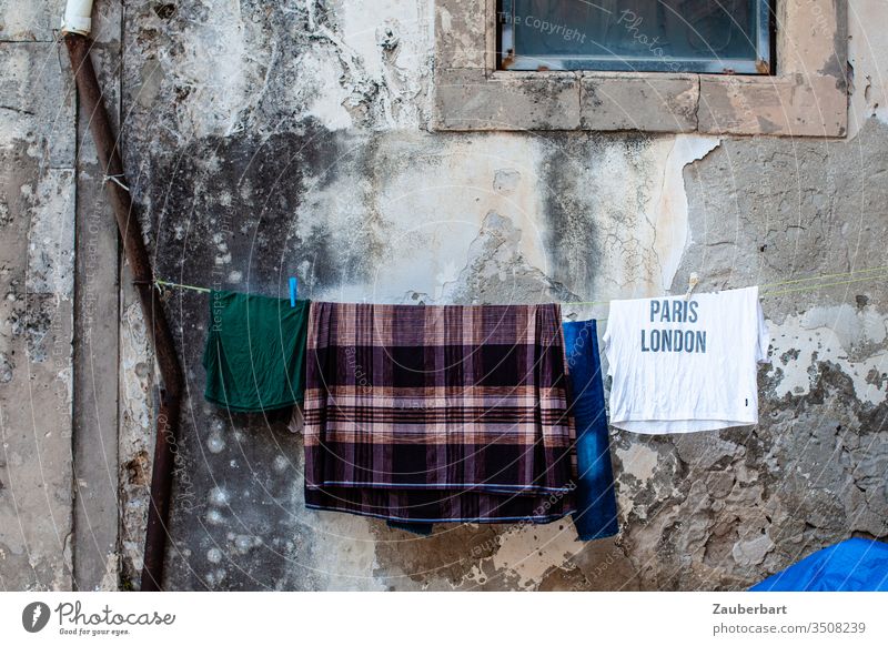 Sehnsucht - T-Shirt mit Aufschrift Paris London hängt mit anderen Wäschestücken auf der Leine vor einer alten Wand in Sizilien Wäscheleine Regenrinne baufällig