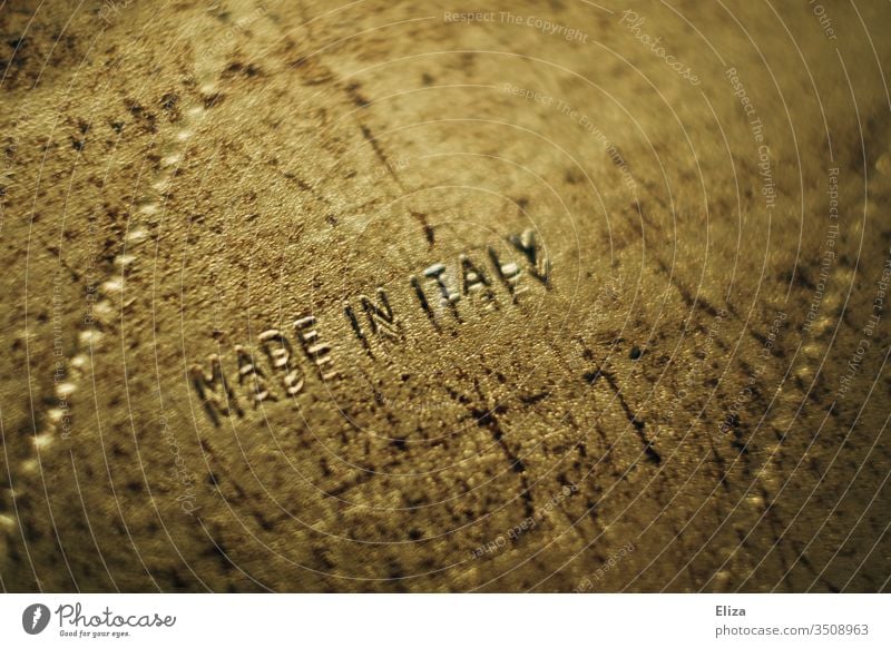 Goldener Gegenstand, auf dem Made in Italy geschrieben steht gold Struktur hergestellt in Italien Produziert produzieren Farbfoto Holz Inszenierung importiert