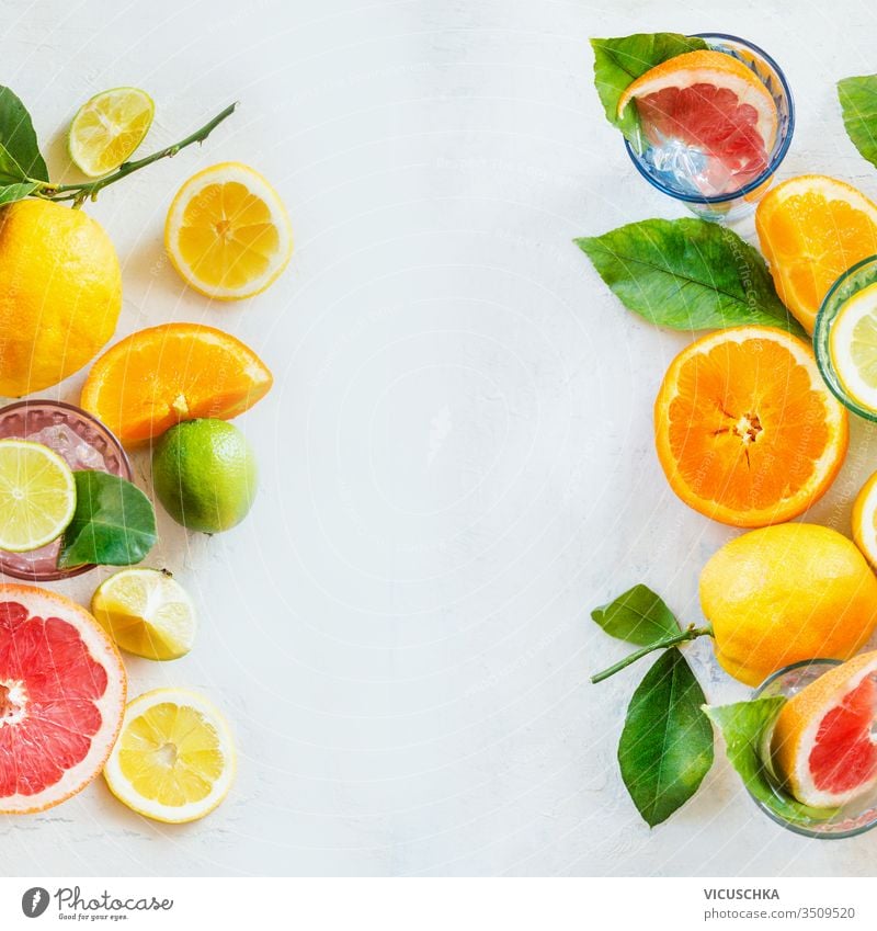 Rahmen aus verschiedenen Zitrusfrüchten mit grünen Blättern auf weißem Tisch, Draufsicht. Gesunde Lebensweise. Inhaltsstoffe. Vitamine. Hälften und Scheiben. Gestaltung