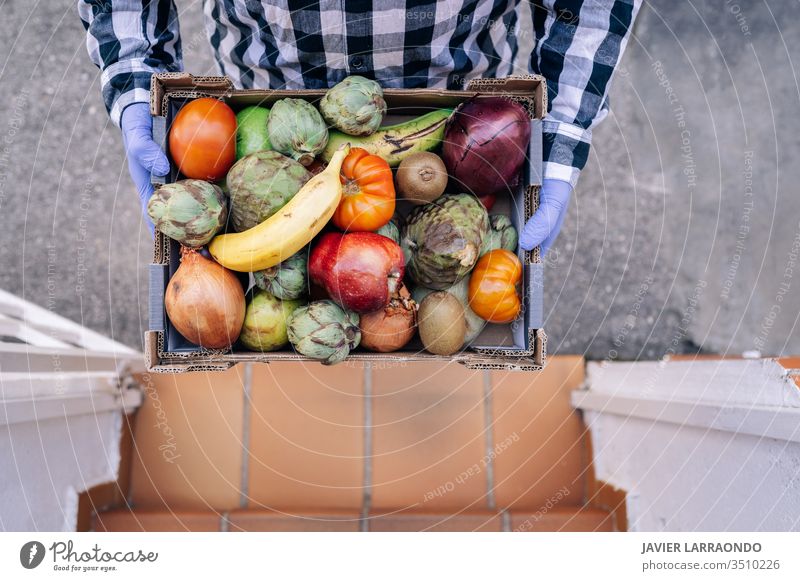 Männlicher Freiwilliger, der eine Kiste mit Gemüse und Obst in einer Haustreppe hält. Freiwilliger Helfer, Abriegelung, Epidemiekonzept Unterstützung