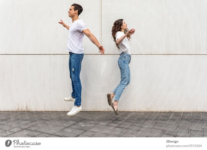 Junges Paar springt Rücken an Rücken gegen weiße Stadtmauer urban Lifestyle jung Kaukasier Frau Mann Glück Großstadt Fröhlichkeit schön Mädchen springend Spaß