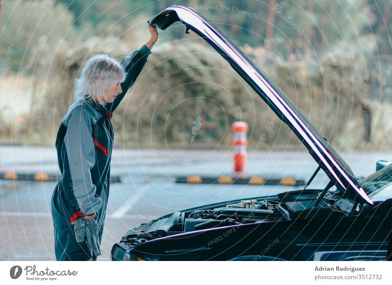 Attraktive junge blonde Frau, die eine Automechaniker-Uniform trägt und das Auto repariert Automobil PKW Kaukasier Reparatur Fahrzeug attraktiv Hintergrund