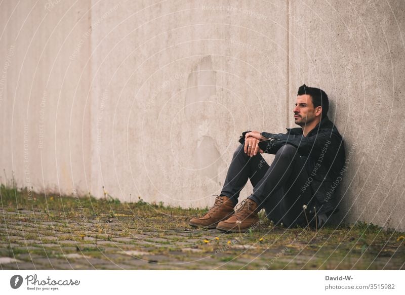 Mann sitzt einsam an einer Wand draußen alleine nachdenklich frustriert Frustration Textfreiraum oben Textfreiraum links Textfreiraum Mitte Model Ruhe sauer
