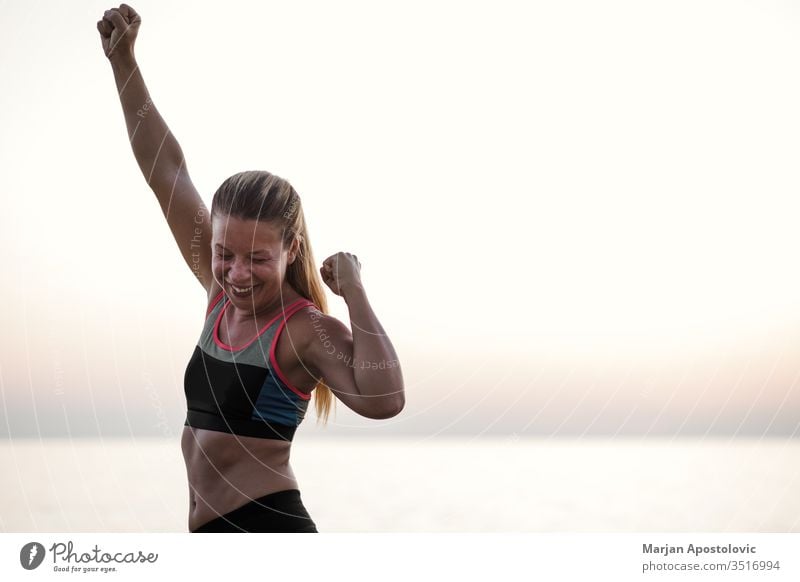 Junge Frau steht mit erhobenen Armen triumphierend am Meer Errungenschaft Aktion aktiv Aktivität Waffen Athlet schön Herausforderung Ausdauer Abend Übung passen