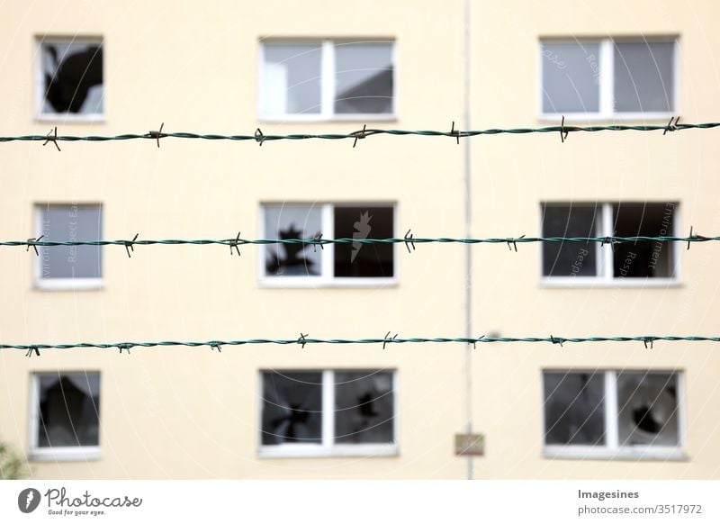 Reihen von Stacheldraht im Hintergrund ein verlassenes Wohngebäude mit zerbrochenen Fenstern. Konzept von Geisterstadt, Isolation und Sicherheit. Gefängnis, Flüchtling, Einsamkeit