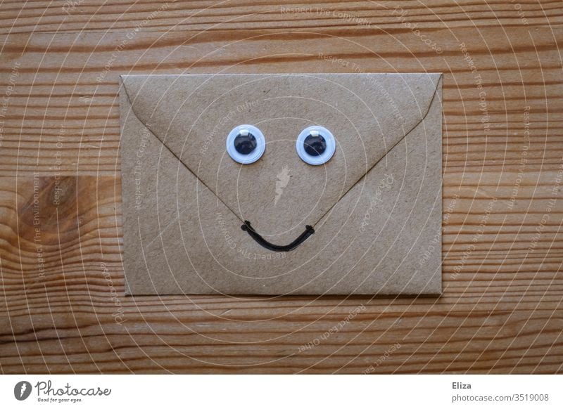 Ein freundlicher Briefumschlag mit Wackelaugen und einem lächelnden Gesicht auf Holz Augen lustig nett post erfreulich Kommunikation Nachricht Post