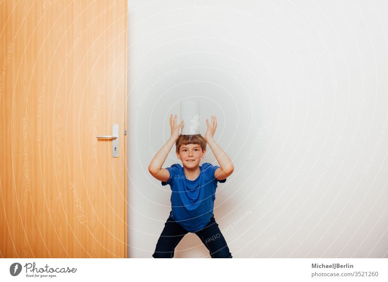 Junge balanciert Toilettenpapier auf dem Kopf übrig Gleichgewicht Kind Korona covid-19 Seuche Spaß Spiel Hamsterer Hamsterkauf heimwärts Ausbruch Pandemie