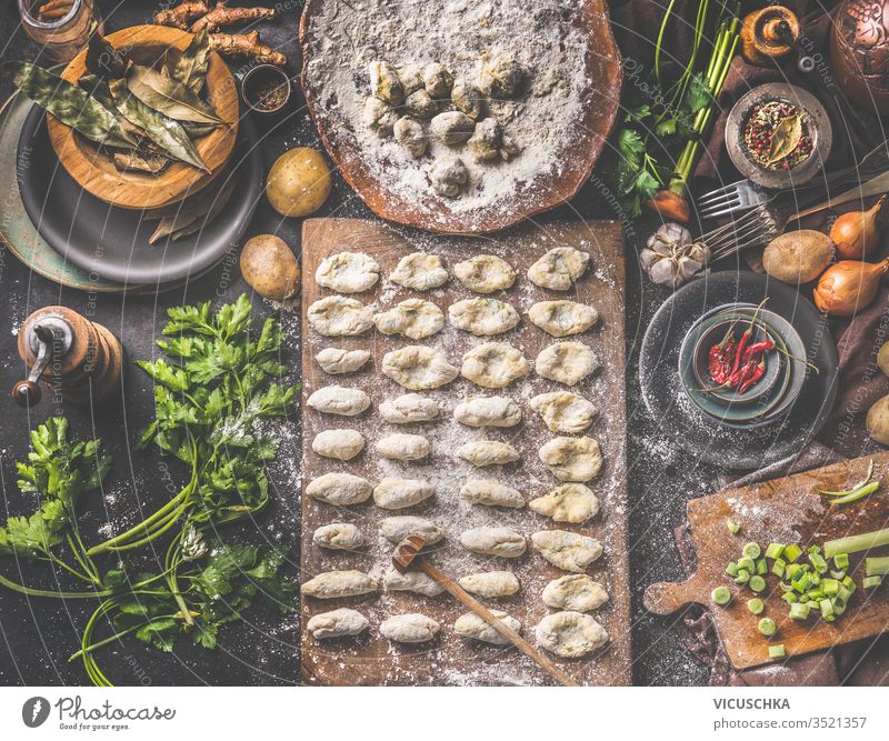 Hausgemachte Gnocchi bei der Zubereitung. Kartoffelteig auf dunklem, rustikalem Küchentisch mit Schneidebrett und gesunden Zutaten. Schmackhafte Hausmannskost. Ansicht von oben. Stilleben