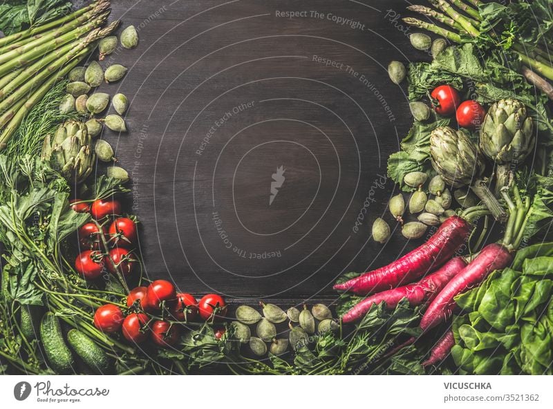 Lebensmittelhintergrund mit einer Gruppe verschiedener frischer Bio-Gemüsesorten aus dem Garten auf dunklem, rustikalem Holzgrund. Ansicht von oben. Gesunde, saubere vegetarische Zutaten: Tomate, Kopfsalat, Wurzelgemüse, Artischocken