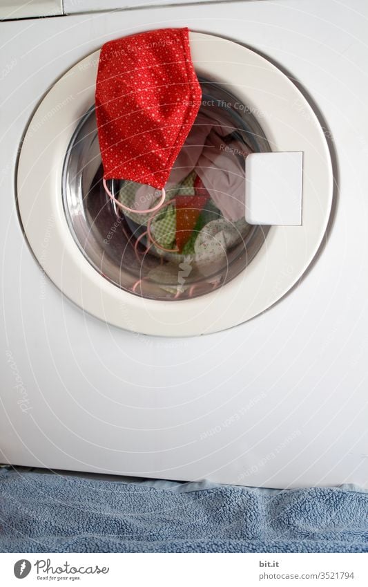 Rote selbstgenähte Schutzmaske aus Stoff mit Punkten, hängt vor der Wäsche, Desinfektion auf der Tür der Waschmaschine im Bad. Steriler Mundschutz zum Schutz vor einer Ansteckung mit Corona, Viren, Grippe, Krankheiten und gegen Smog, Luftverschmutzung.