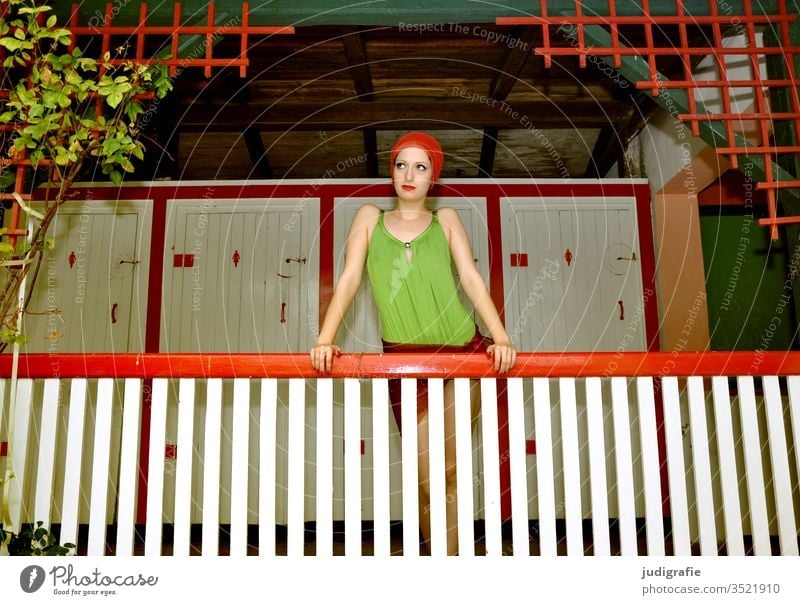 Das Mädchen mit der schönen roten Badekappe und grünem Badeanzug stützt sich auf das Geländer der Damenumkleide. Eine Sommerliebe. Frau Badebekleidung Badehaube