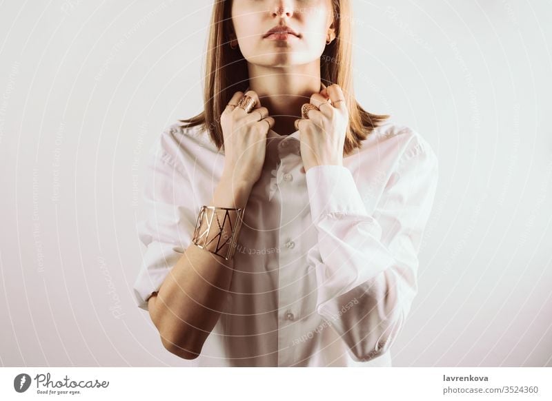 Porträt einer jungen erwachsenen Frau, die mit ihren Händen einen Kragen eines weißen Hemdes hält, selektiver Fokus Ringe gesichtslos Schmuck Atelier Armband
