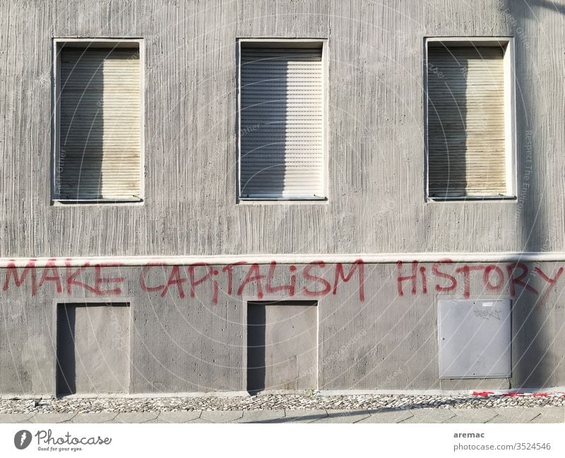 Graue Hauswand mit geschlossen Fensterläden und Aufschrift grau Kapitalismus Make capitalism history Kritik Fassade Spruch Slogan Wand Menschenleer Mauer