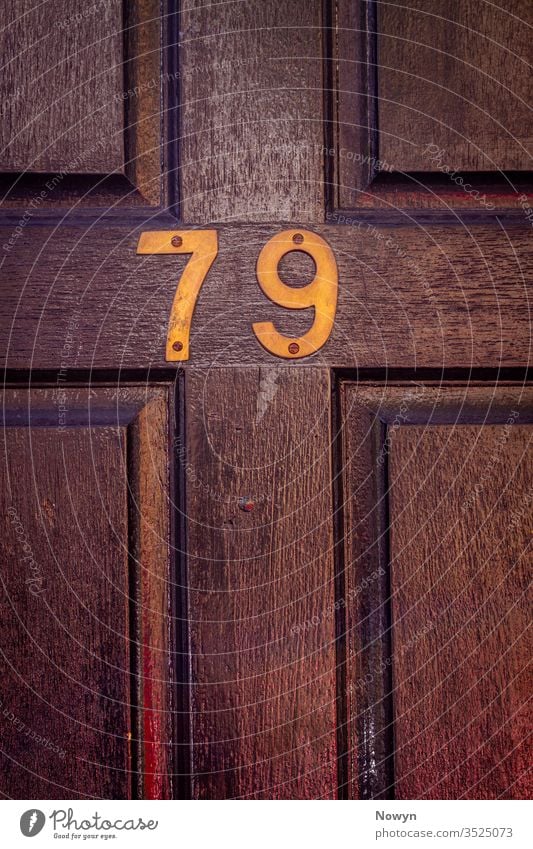 Hausnummer 79 an einer dunklen hölzernen Haustür 79 Zahl Adresse gealtert britannien klassisch stilvoll abschließen Nahaufnahme dunkel Dekoration & Verzierung