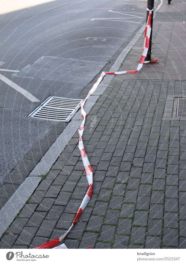 Flatterband entlang der Strasse und dem Bürgersteig auf dem Boden liegend Absperrung Straße Markierungslinie Gully Pflastersteine Fahrbahnrand Rinnstein