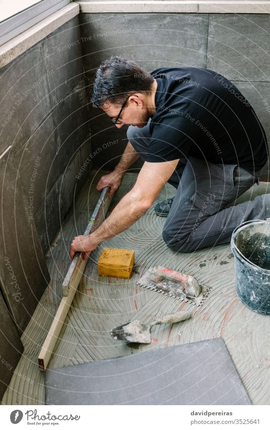 Maurer-Prüfboden mit einer Ebene Handwerker Nivellierung Überprüfung Boden Kacheln Renovierung sicherstellen Niveau Zement-Fliesenimitation verglaste Terrasse