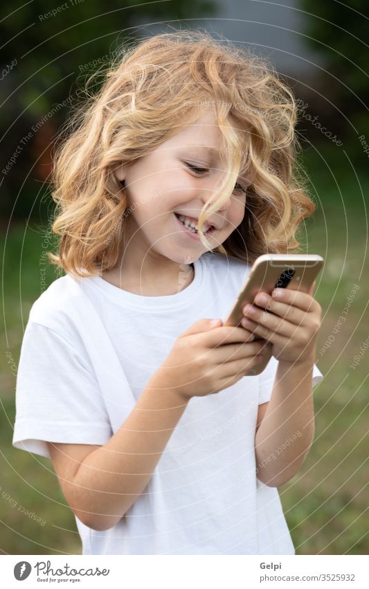 Lustiges Kind mit langen Haaren, das ein Handy hält. Telefon Park Freizeit Funktelefon Kindheit Smartphone Lifestyle Junge blond Mitteilung Anschluss