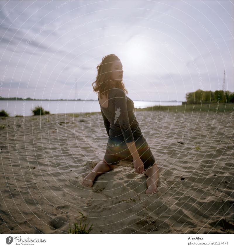 analoges rückwärtiges Portrait einer jungen Frau im Kleid am Strand beim Sonnenuntergang Mädchen schön groß sportlich schlank fit brünett Locken langes Haar