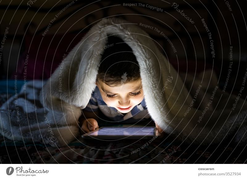 Kleines Kind benutzt eine mit einer Decke bedeckte Tablette allein Anwendung Bett Schlafzimmer Schlafenszeit Junge Kindheit Nur für Kinder spielende Kinder