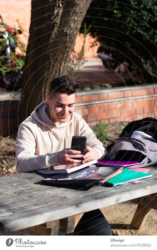 Junge Studentin, die in einem Park sitzt, während sie ein Mobiltelefon auf einem Holztisch benutzt eine Person Schüler Telefon Tisch Sitzen Mitteilung