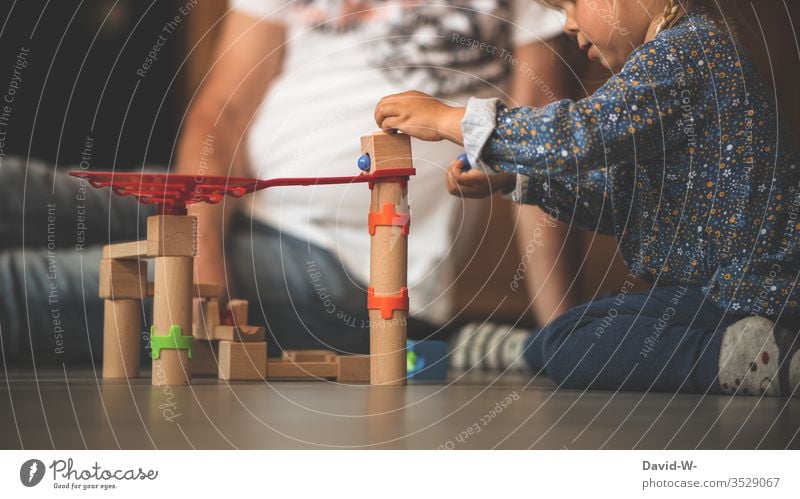 Kind spielt mit Holzspielzeug Spielzeug spielen Kinderzimmer Vater sitzen hocken drinnen Murmeln bauen kreativ spaß freude fröhlich konzentriert vorsichtig
