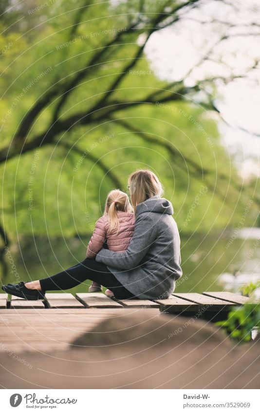 Mutter sitzt mit Kind auf einem Steg am Ufer eines Sees Mädchen Natur natürlich Familie Eltern Kindheit niedlich Liebe geborgenheit Ruhe verantwortung zusammen