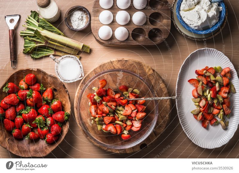 Frische Erdbeeren und Rhabarber auf hölzernem Tischhintergrund mit Zutaten für schmackhaftes saisonales Kochen oder Backen. Ansicht von oben. Gesundes und sauberes Essen. Paläo-Diät. Hausmannskost. Gartenfrüchte essen