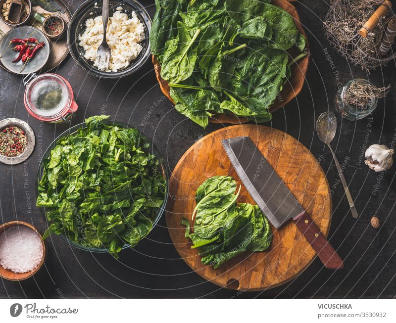 Zubereitung eines köstlichen vegetarischen Spinatgerichts. Schneidebrett mit Messer auf rustikalem Küchenhintergrund.  Gesunde Zutaten . Ansicht von oben.
