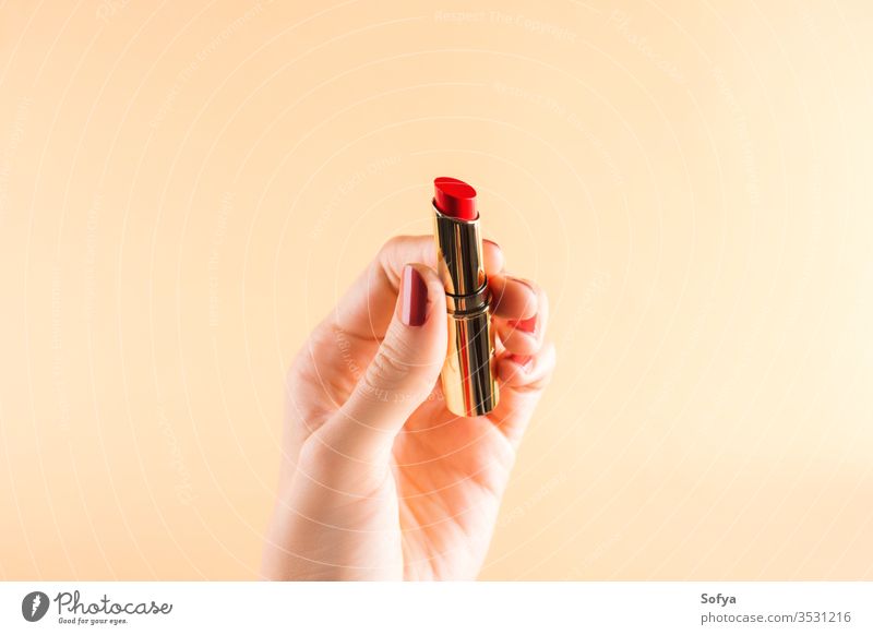 Weibliche Hand hält roten Lippenstift auf hellorangem Glamour Schönheit Frau Mode Farbe schön Make-up Nahaufnahme Accessoire Nägel Personal Mädchen Finger