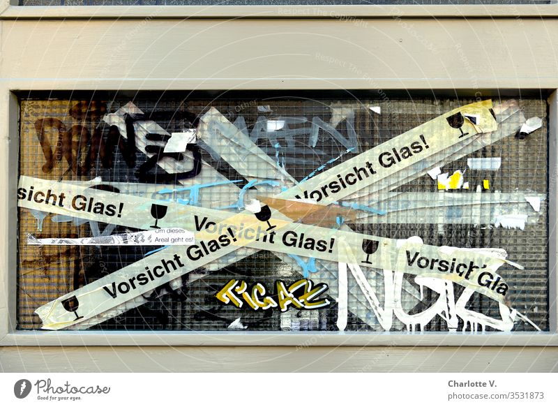 Vorsicht Glas | eine zerbrochene Fensterscheibe wird mit "Vorsicht-Glas-Tape" zusammengehalten und zusätzlich von Graffiti verschönert. Glasscheibe