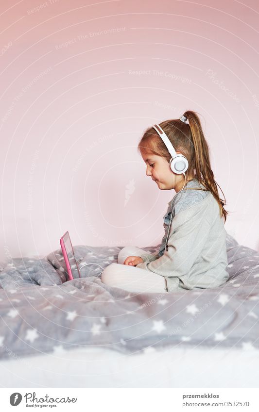 Kleines Mädchen im Vorschulalter lernt online Rätsel lösen und spielt zu Hause Lernspiele auf Tablet Kind zuschauend hören Lernen lehrreich Geduldsspiel Bett