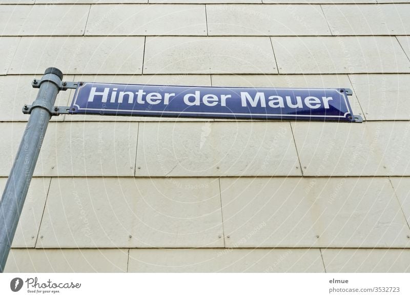 blaues Straßenschild "Hinter der Mauer" vor einer grauen Fassade Straßenname Hinweis Schild Beschilderung Wand Schilder & Markierungen Hinweisschild