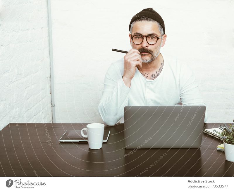 Erwachsener Mann arbeitet zu Hause am Laptop Arbeit freiberuflich benutzend Konzentration Quarantäne zur Kenntnis nehmen COVID19 Kopfbedeckung Brille männlich