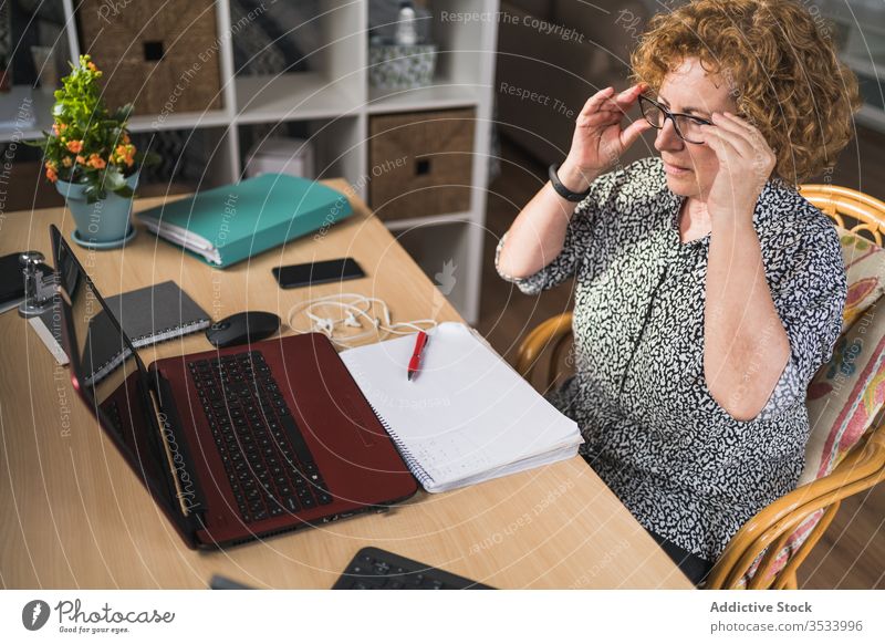 Nachdenkliche erwachsene Frau, die Musik über Kopfhörer hört, während sie zu Hause am Laptop arbeitet ruhen heimwärts Entfernung Arbeit abgelegen Pause genießen
