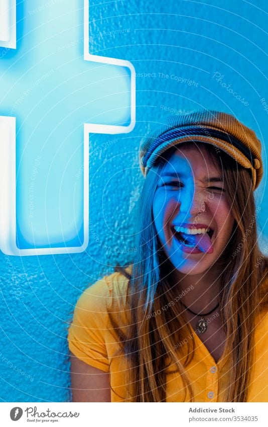Junge fröhliche Frau mit lustigem Gesicht auf blauem Hintergrund Zunge zeigen neonfarbig auflehnen ausspannen Gesicht machen Spaß haben Grimasse Zeichen gelb