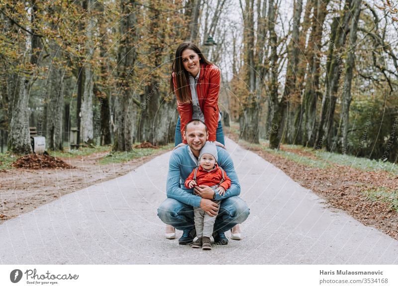 Glückliches Familien-Stil-Paar mit 1-jährigem Kind, das in rot-blauer Kleidung im Park lächelt schön Pflege Kaukasier heiter Kindheit Konzept niedlich Papa Papi