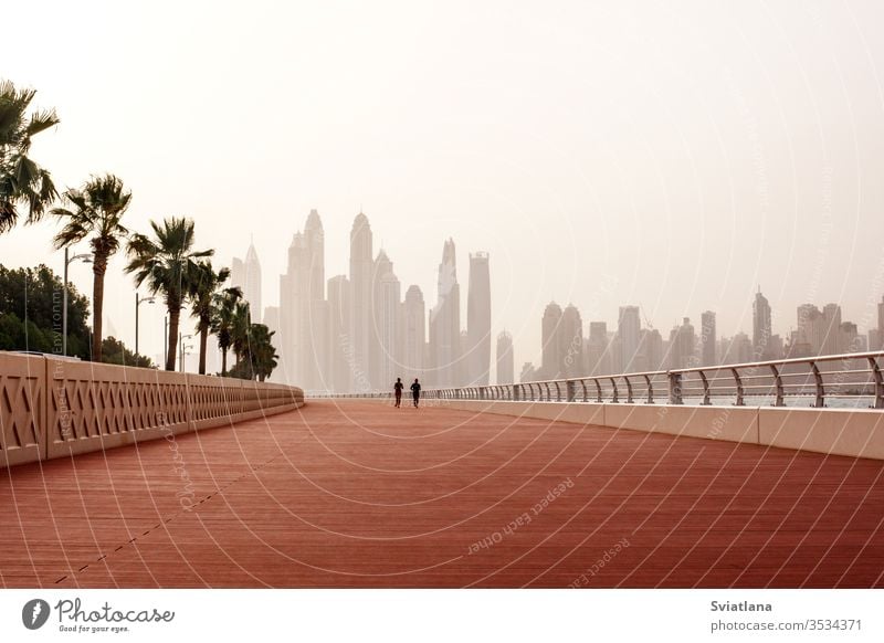 Morgens laufen ein Mann und eine Frau die Straße entlang, mit einem wunderschönen Blick auf Dubai. VEREINIGTE ARABISCHE EMIRATE Wellenbrecher Steine MEER Strand
