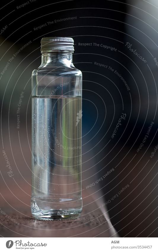 Klarglasflasche mit Wasser aqua Hintergrund Getränk schwarz Flasche in Flaschen abgefüllt braun Verschlussdeckel Sauberkeit übersichtlich Nahaufnahme Container