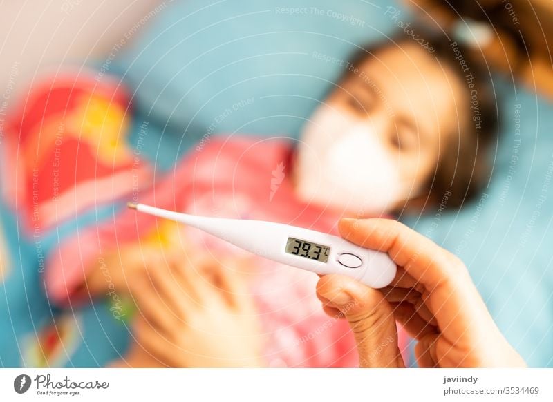 Die Mutter misst die Temperatur ihres Kleinkindes, geschützt durch eine Maske. Thermometer Mädchen Fieber Tochter Kaukasier Menschen Pflege Krankheit Grippe