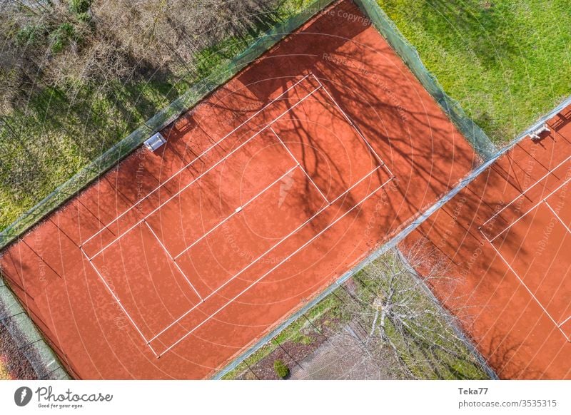 ein Tennisplatz von oben Sport Tennisplätze Asche orange weiß Linien Sonne Schatten Sommer Winter stechend Tennisnetz Tennisnetze Ball Bälle Tennisball Bäume